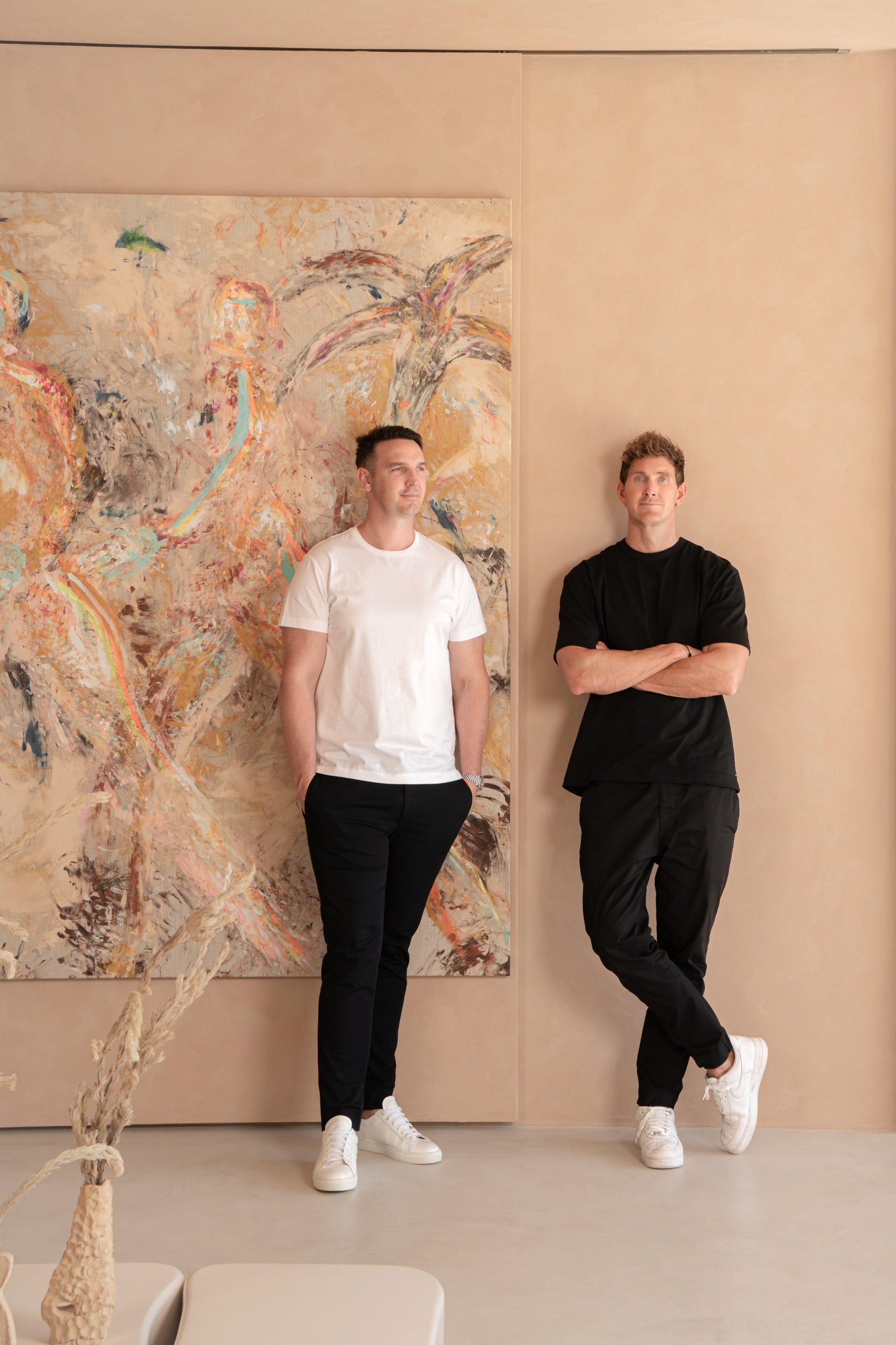 Two founders standing against an abstract painted wall. Graya